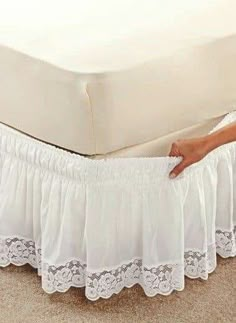 a woman is holding the edge of her bed skirt to show it's lace trim