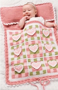 a baby laying on top of a blanket next to a pink and green blanket with hearts