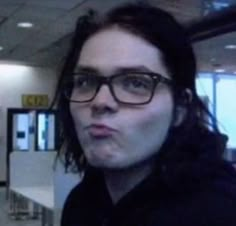 a woman wearing glasses is standing in an airport terminal looking at the camera and making a funny face