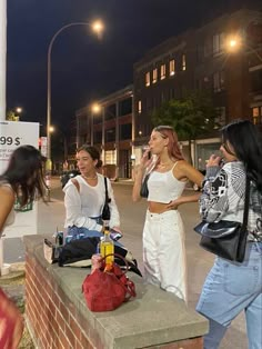 three women are standing on the side walk talking to each other and one is holding a cell phone