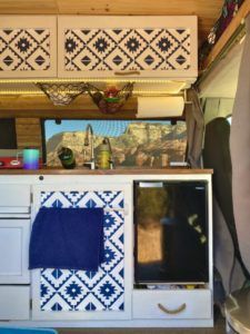 the interior of a camper with blue and white tiles on the walls, cupboards and sink