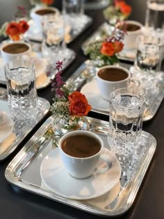 there are cups and saucers on the table with silver trays holding glasses and flowers