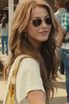 a woman with sunglasses is walking down the street in front of some people and holding onto a handbag