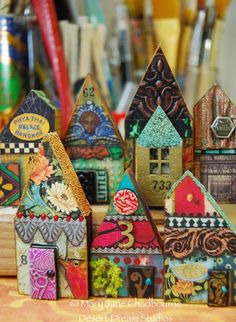 small wooden houses are lined up on a table with pens and pencils in the background