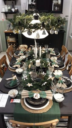 a dining room table set for christmas with green and white decorations on it, surrounded by holiday greenery