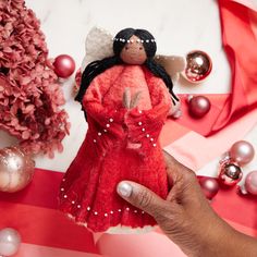 a hand holding a red cloth doll next to ornaments