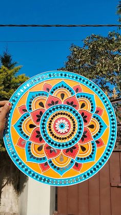 a person holding up a colorful plate in front of a building with trees and power lines