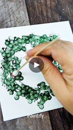 someone is painting a wreath with green paint on white paper and holding a pencil in their left hand