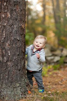 a little boy standing next to a tree in the woods