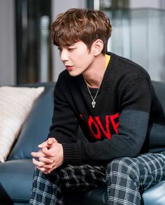 a young man sitting on top of a couch wearing plaid pants and a black sweater