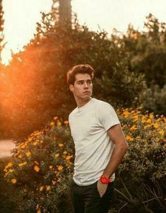 a young man standing in front of flowers with a butterfly flying above him and the sun behind him