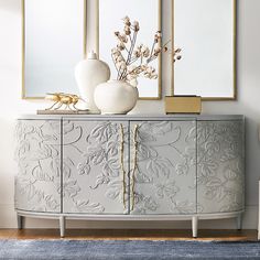 a white and gold sideboard with two vases sitting on it's sides