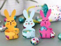 some paper rabbits sitting next to each other with eggs in front of them on a table