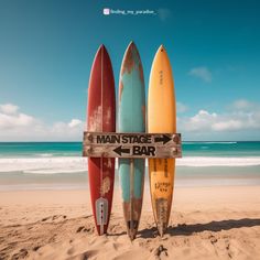 three surfboards leaning up against a sign on the beach that says mantasge bar