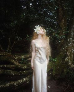 a woman in a white dress standing next to a tree with flowers on her head