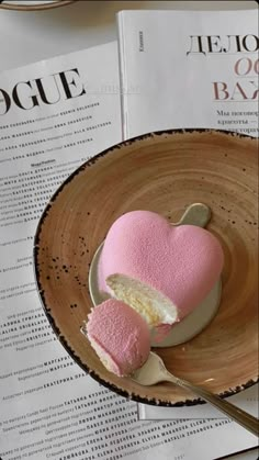 a pink heart shaped cake in a wooden bowl on top of a table next to a magazine