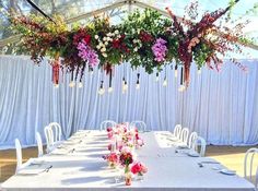 the table is set up with white chairs and flowers hanging from the ceiling over it