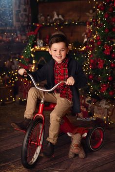 a young boy is sitting on a red bike in front of a christmas tree and presents