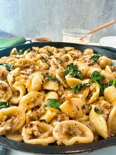 a skillet filled with pasta and spinach on top of a table next to a glass of milk