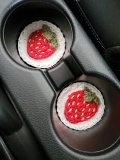 two crocheted strawberries are sitting in the center console of a car seat