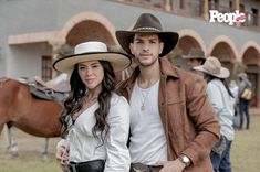 a man and woman standing next to each other in front of a building with horses