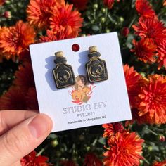 a person holding up a pair of earrings in front of some red and orange flowers