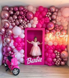 a pink scooter parked in front of a wall with balloons and a barbie doll