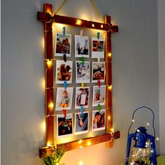 a wooden frame hanging on the wall with pictures and string lights around it, along with a potted plant