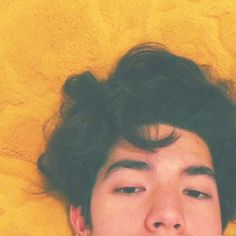 a young man laying on top of a yellow blanket holding a cell phone to his ear