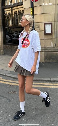 a woman is walking down the street in short skirt and white t - shirt with an orange sticker on it