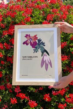 a person holding up a framed poster in front of red flowers