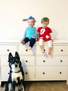 two young children sitting on top of a dresser next to a black and white dog