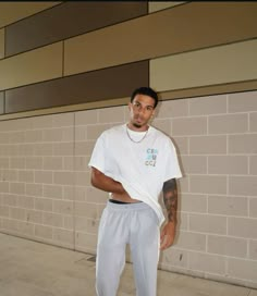 a man standing in front of a brick wall wearing white pants and a t - shirt