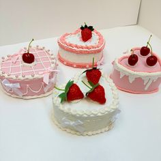 four cakes decorated in pink and white with cherries on the top one has a heart shaped cake