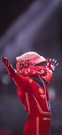 a man in red is holding his hands up to the sky and wearing a helmet with numbers on it