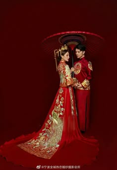 two people dressed in red and gold holding an umbrella