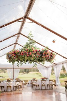 the inside of a tent with tables, chairs and flowers hanging from it's ceiling