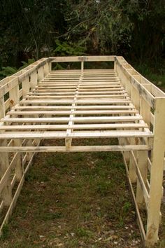 a wooden bed frame sitting in the middle of a field with trees in the background