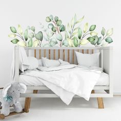 a baby's room with a white bed and green leaves on the wall behind it