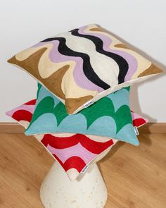 three pillows stacked on top of each other in front of a white vase with wood flooring