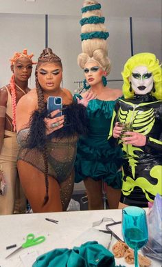 three women dressed up in costumes taking a selfie with their cell phones at a halloween party