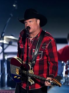 a man wearing a cowboy hat and holding a guitar on stage with other musicians in the background