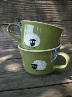 two green mugs with sheep painted on them sitting on a wooden table next to each other