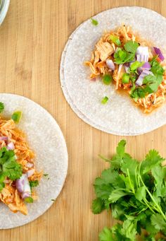 two tortillas topped with chicken and cilantro on top of a wooden table