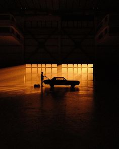 a car is parked in an empty parking garage at night with the headlights on and a person standing next to it