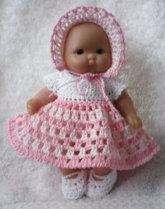 a baby doll wearing a pink dress and bonnet on a white blanket with crochet