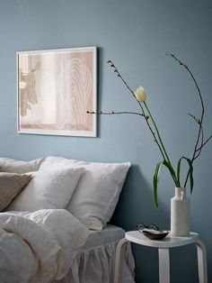 a white bed sitting next to a vase with flowers in it on top of a table