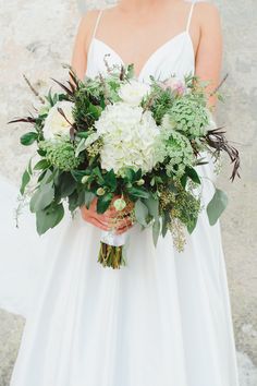 a woman in a white wedding dress holding a bouquet with green and white flowers on it