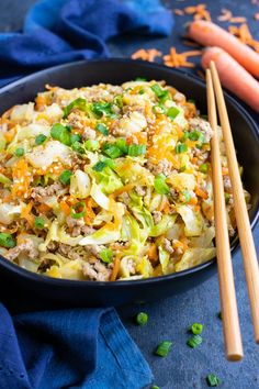 a bowl filled with cabbage and carrots next to chopsticks on a blue cloth