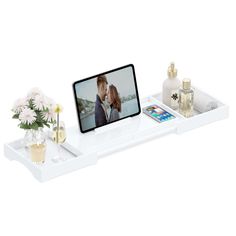 a white shelf with flowers, perfumes and a cell phone on top of it